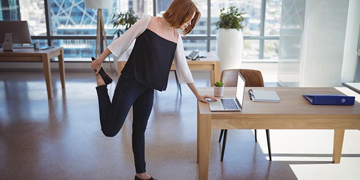 woman standing at her desk stretching as part of workplace wellness